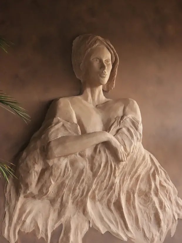 Relieve escultórico de una mujer con los brazos cruzados y vestido drapeado